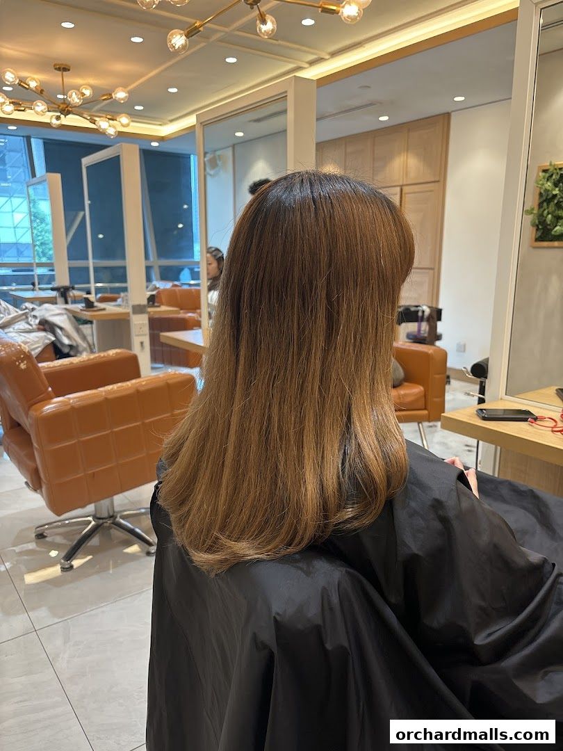 A person sits in a salon chair, draped in a black cape, with their long brown hair visible.