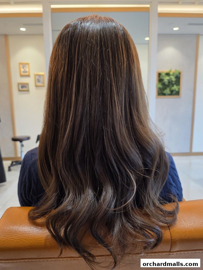Back view of a woman with long, wavy, highlighted brown hair in a salon.
