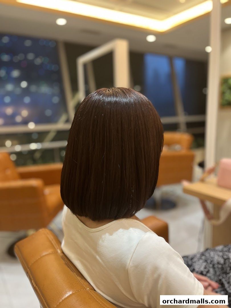 A person with a fresh bob haircut sits in a salon chair with a city view.