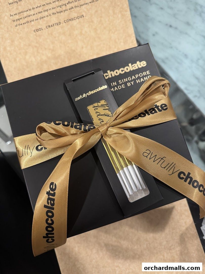 A black gift box from Awfully Chocolate, tied with a gold ribbon, containing chocolate bars.