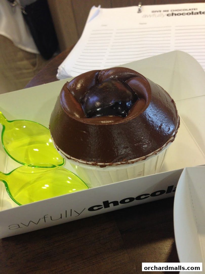 A decadent chocolate cupcake with glossy frosting and a cherry on top, served with bright green spoons.