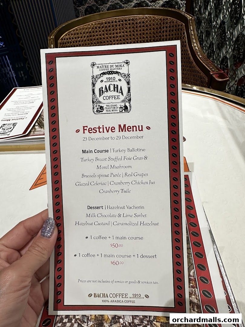 A hand holds a festive menu from Bacha Coffee, detailing main courses and desserts.