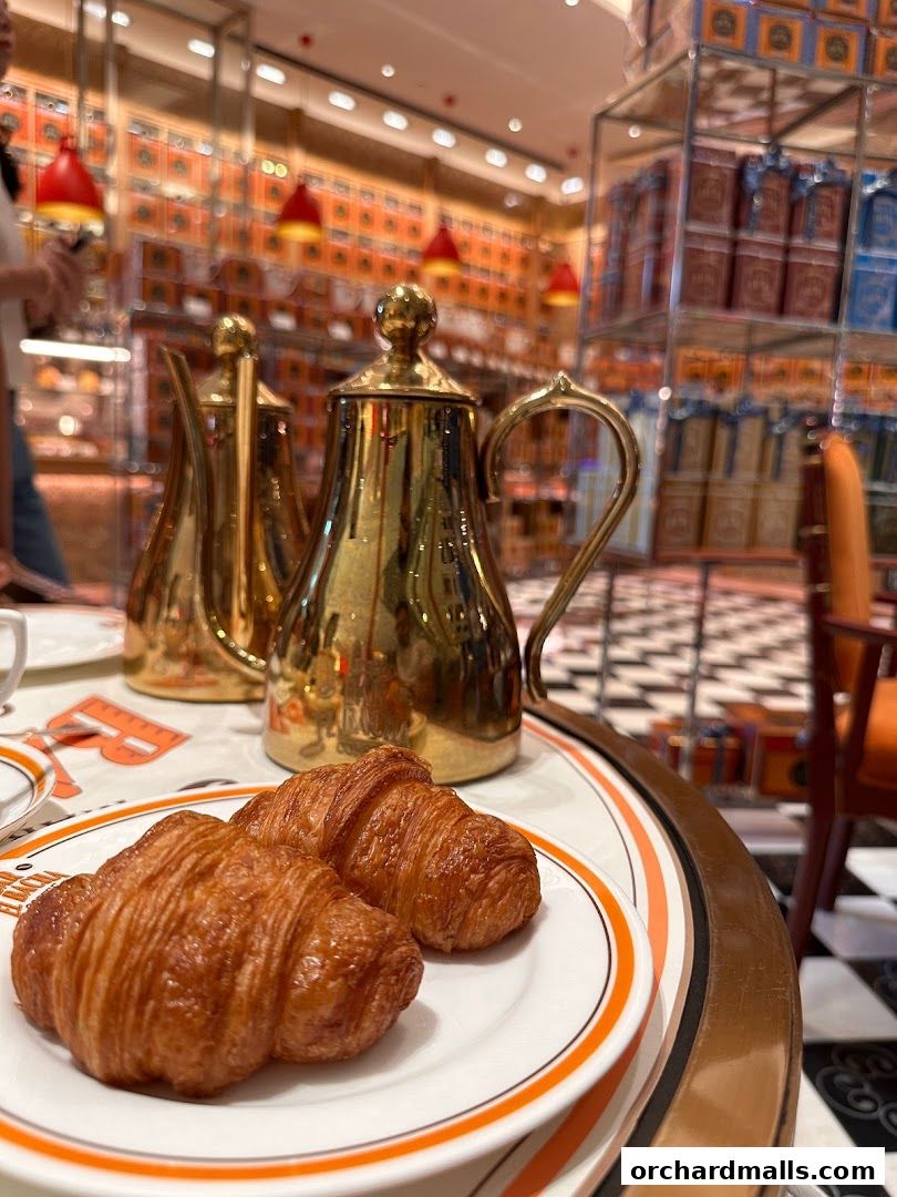 Two golden croissants served with a golden coffee pot on a table at Bacha Coffee.