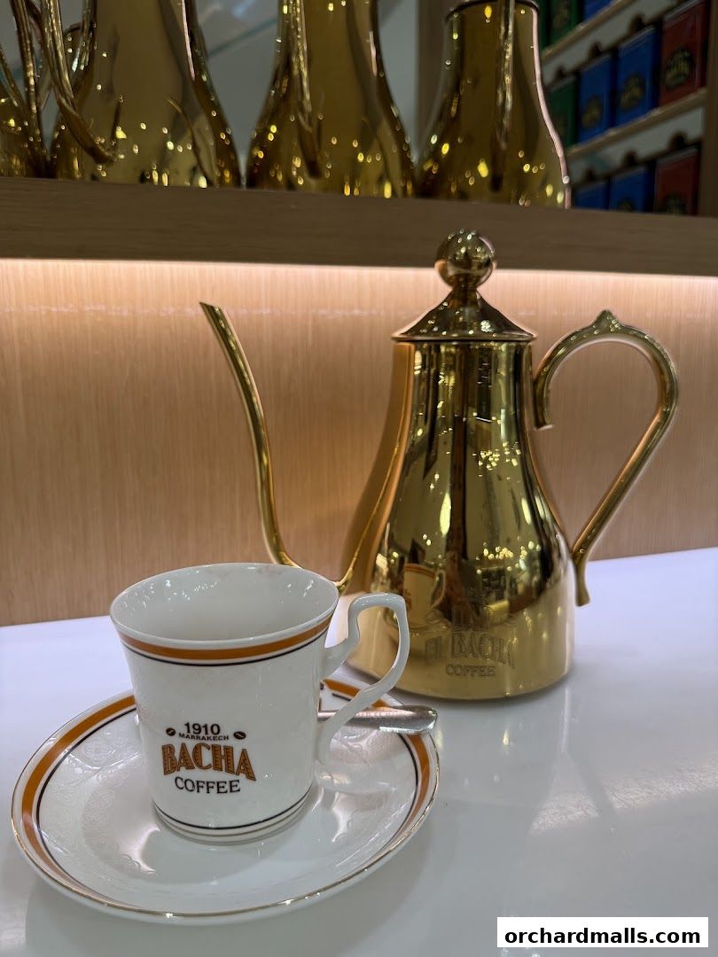 A golden coffee pot and a Bacha Coffee cup and saucer on a white surface.