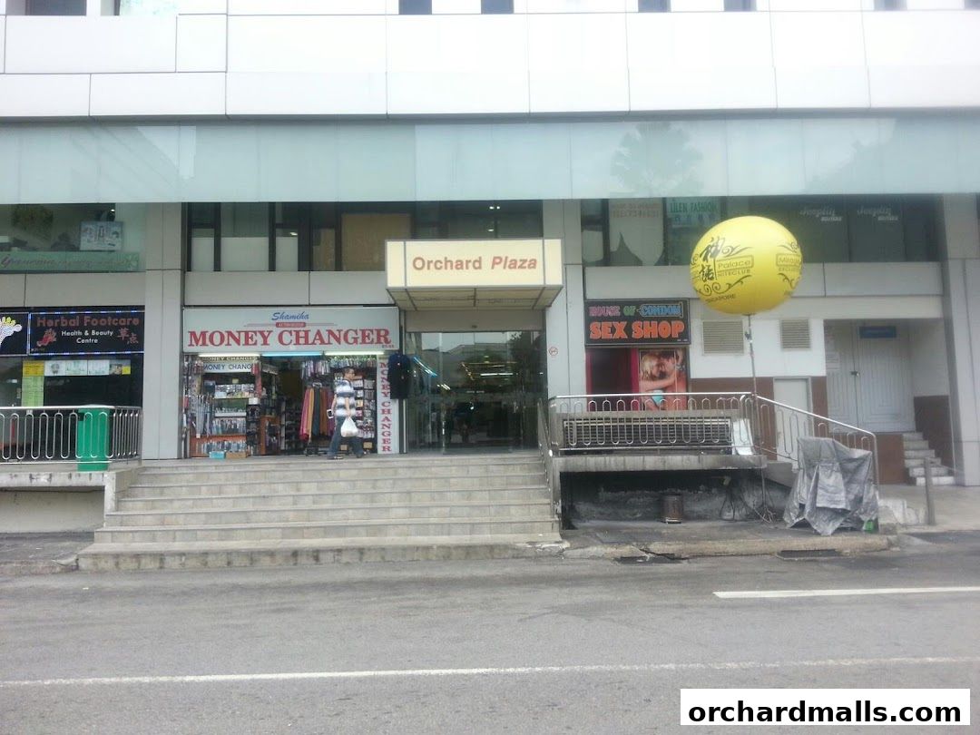 Exterior view of Orchard Plaza with various shops including a money changer and a sex shop.