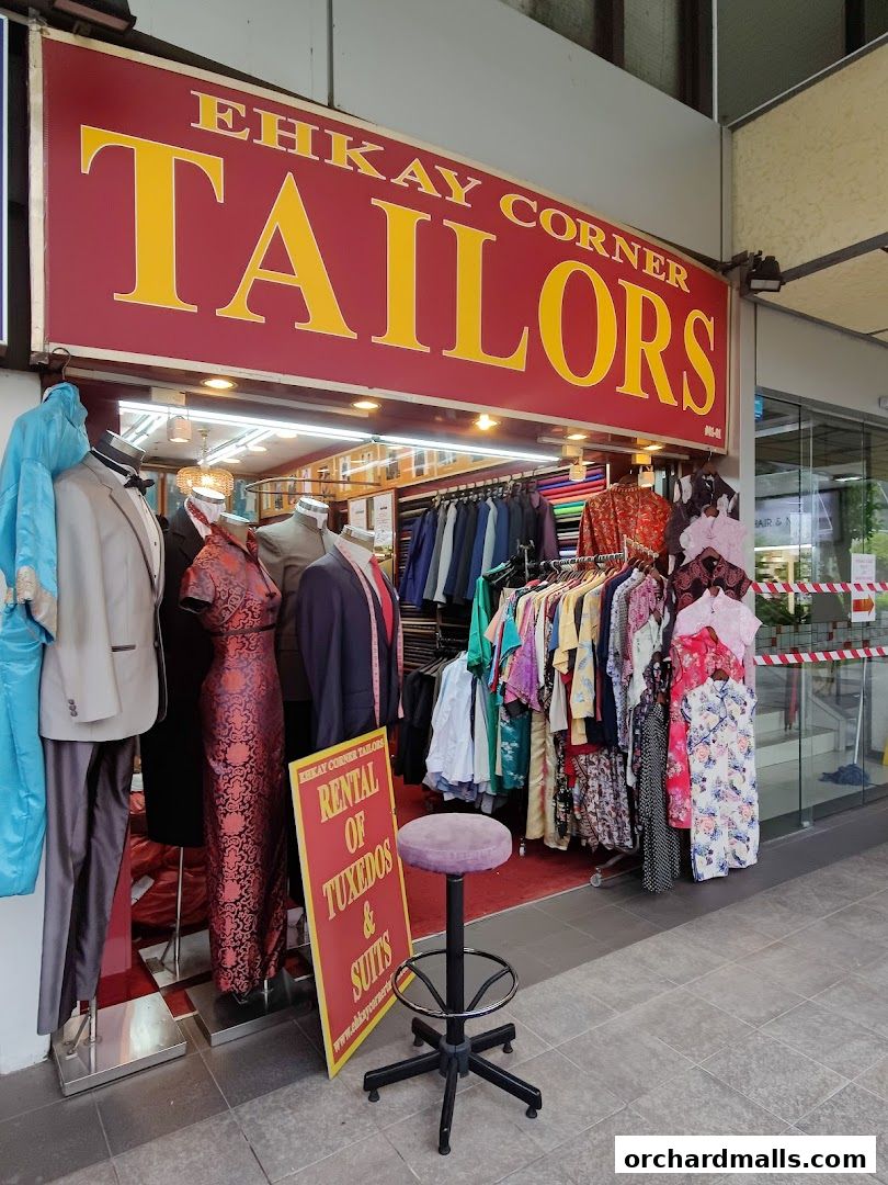 A tailor shop with a display of suits, dresses, and fabrics, and a sign for tuxedo rentals.