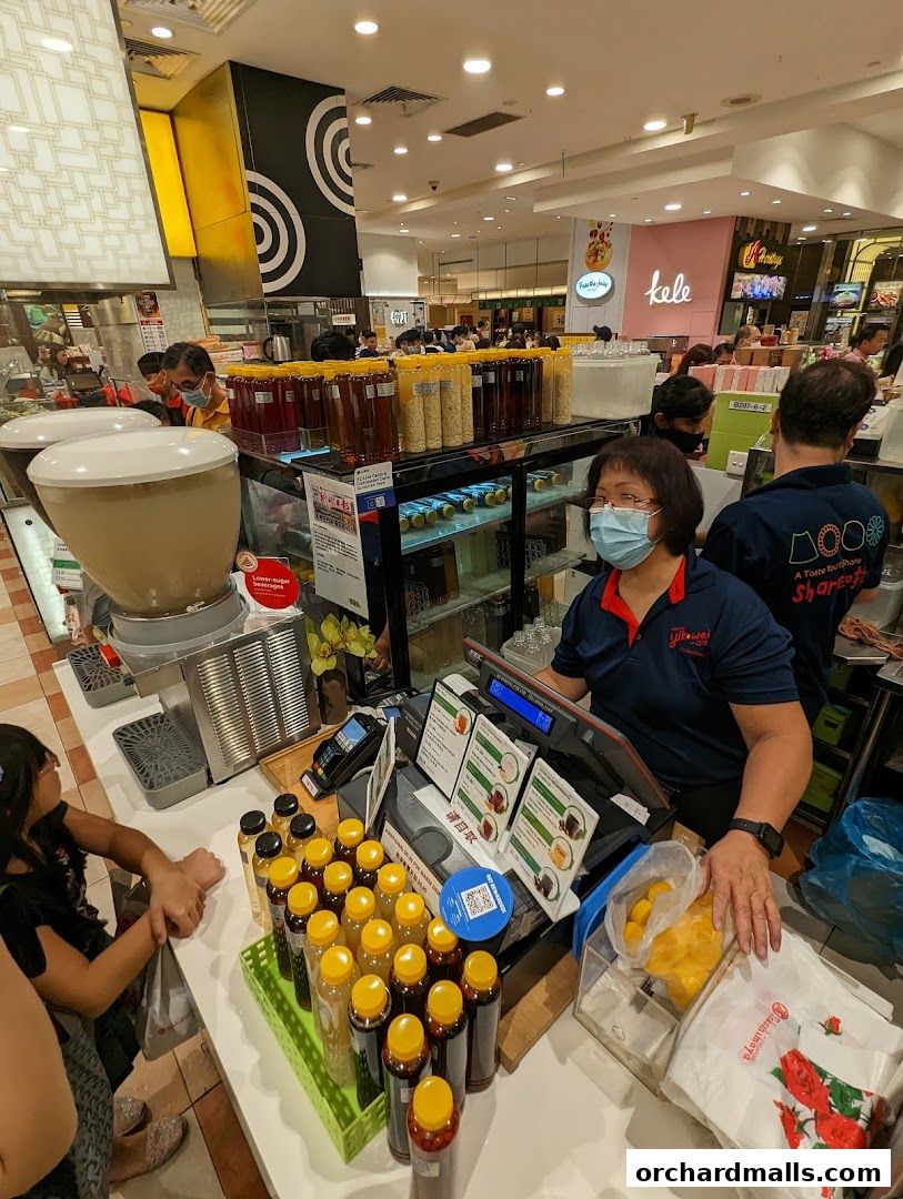 A shop counter with various bottled drinks and a cashier serving customers.