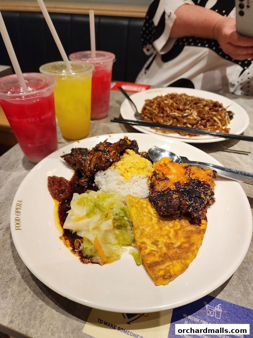 A plate of Indonesian BBQ with rice, vegetables, and a fried omelet, alongside three colorful drinks.