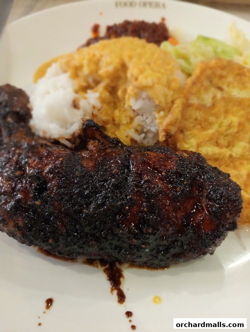 A plate of Indonesian BBQ chicken with rice, egg, and vegetables.