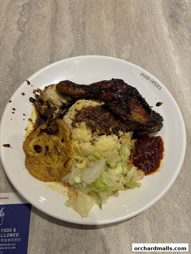 A plate of Indonesian BBQ chicken with rice, fried egg, vegetables, and chili sauce.