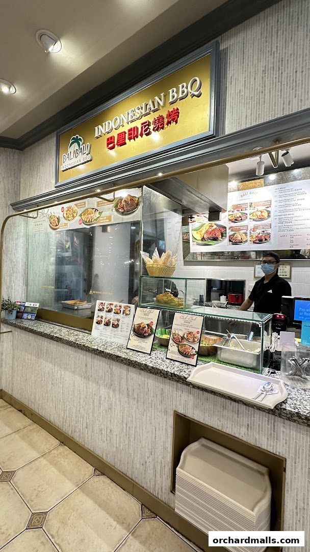 A counter at BaliBali Indonesian BBQ with food displays and a staff member.