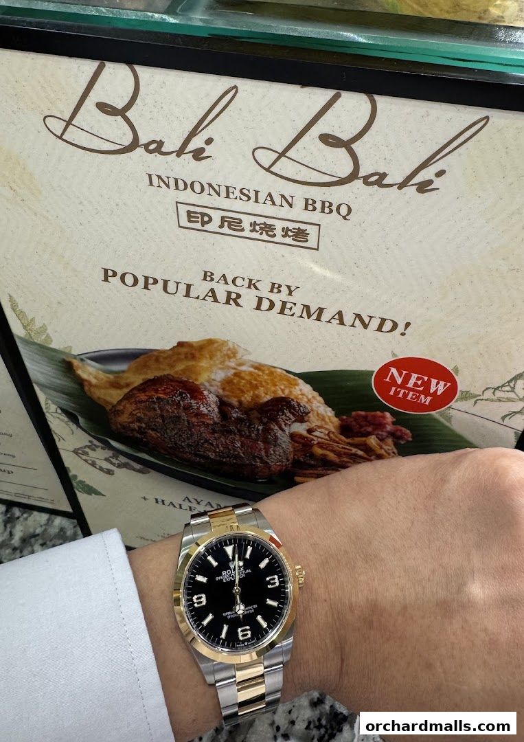 A person's wrist with a watch in front of a sign for Bali Bali Indonesian BBQ.