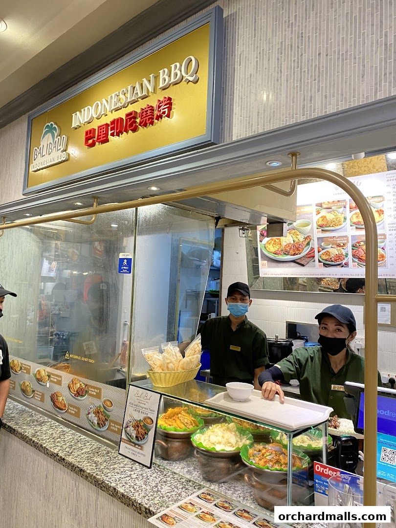 Two staff members stand behind the counter at BaliBali Indonesian BBQ, with food displays and menus visible.