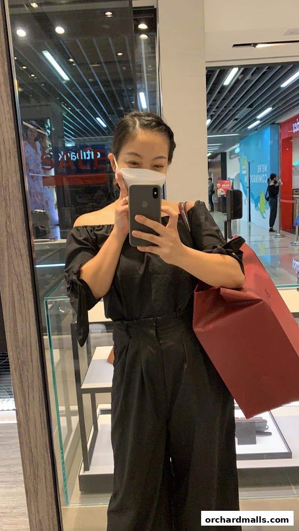 A woman in a black outfit takes a selfie in a Bally store, holding a shopping bag.