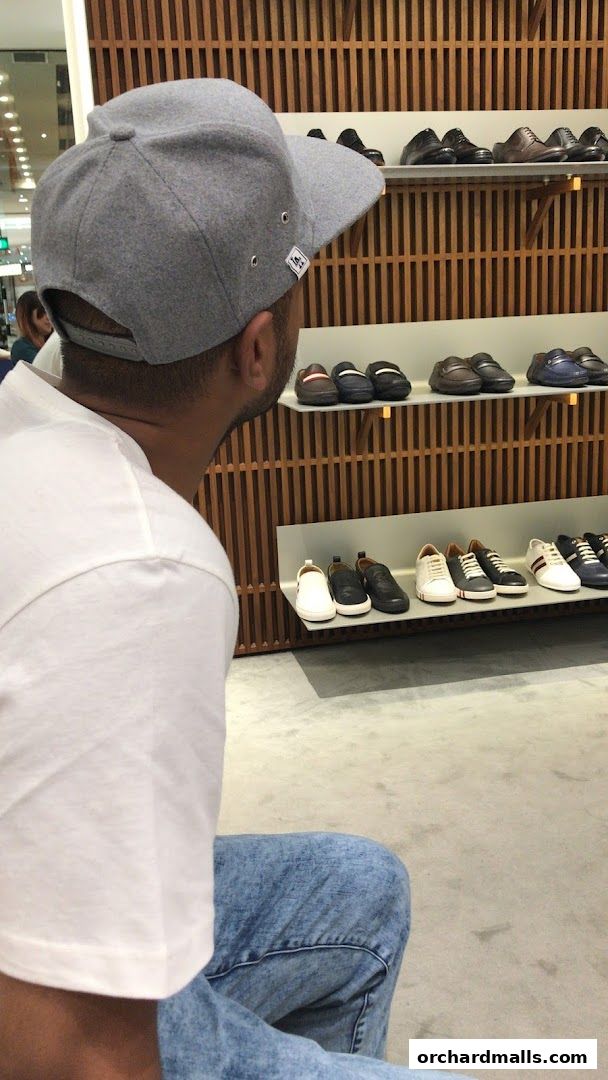 A person wearing a grey cap and white t-shirt looks at shoes displayed on shelves.