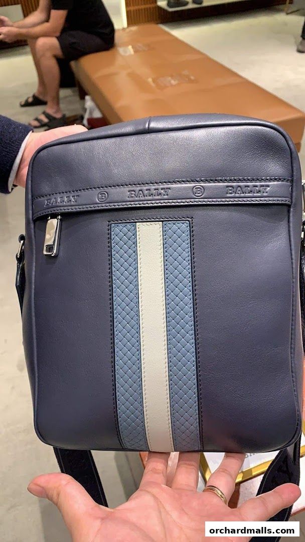 A close-up of a navy blue Bally crossbody bag with signature stripe detail.