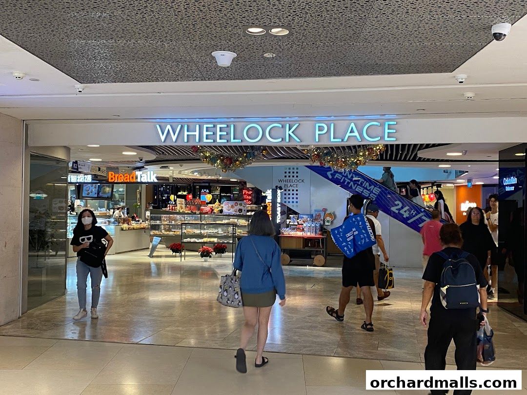 Entrance to Wheelock Place mall with various shops and people walking by.