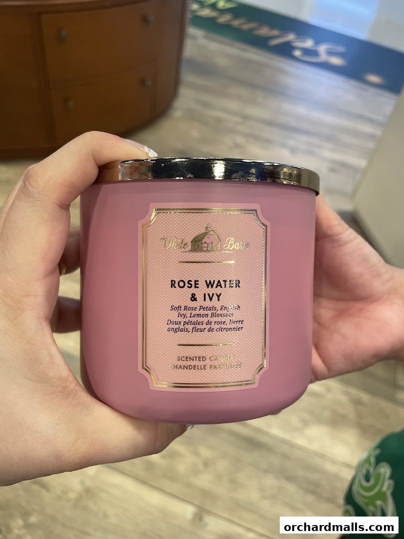 A person holds a pink scented candle with a label for 'Rose Water & Ivy'.