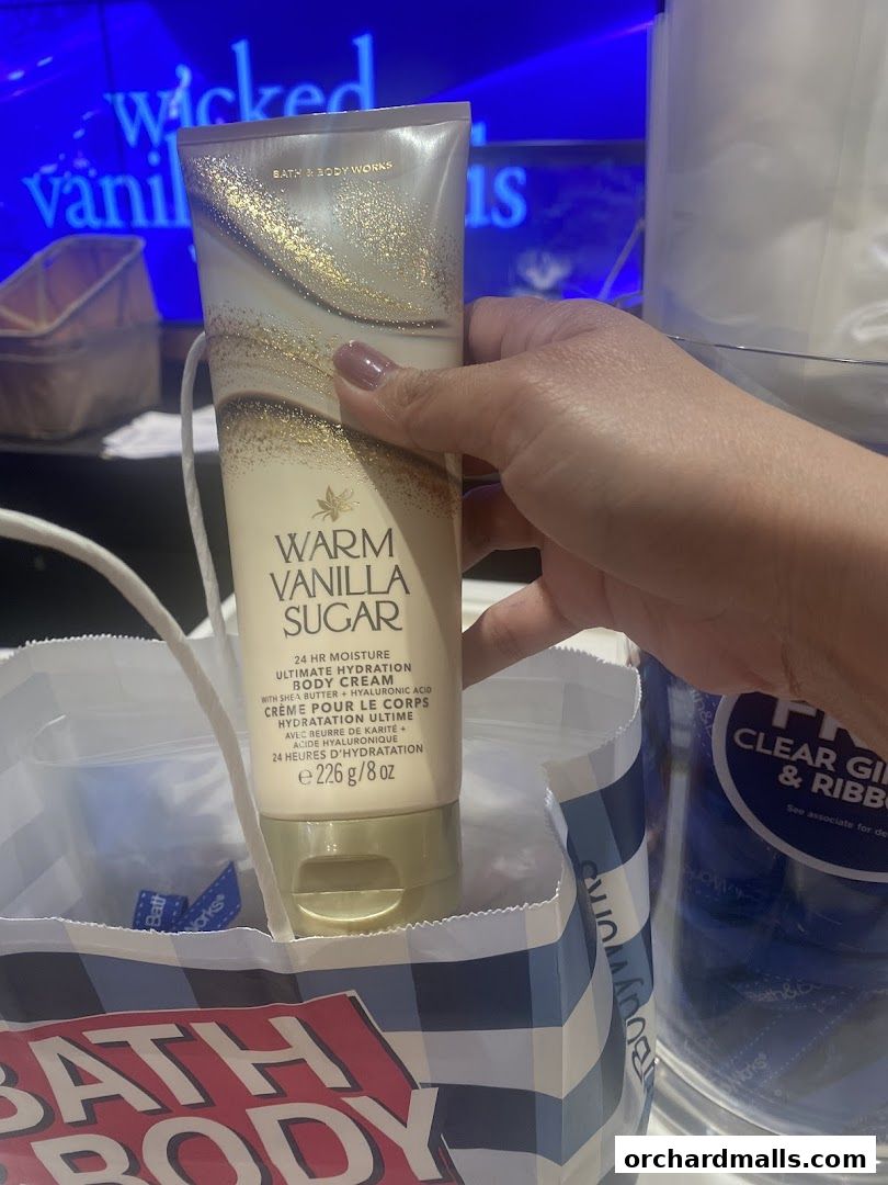 A hand holds a Bath & Body Works Warm Vanilla Sugar body cream above a shopping bag.