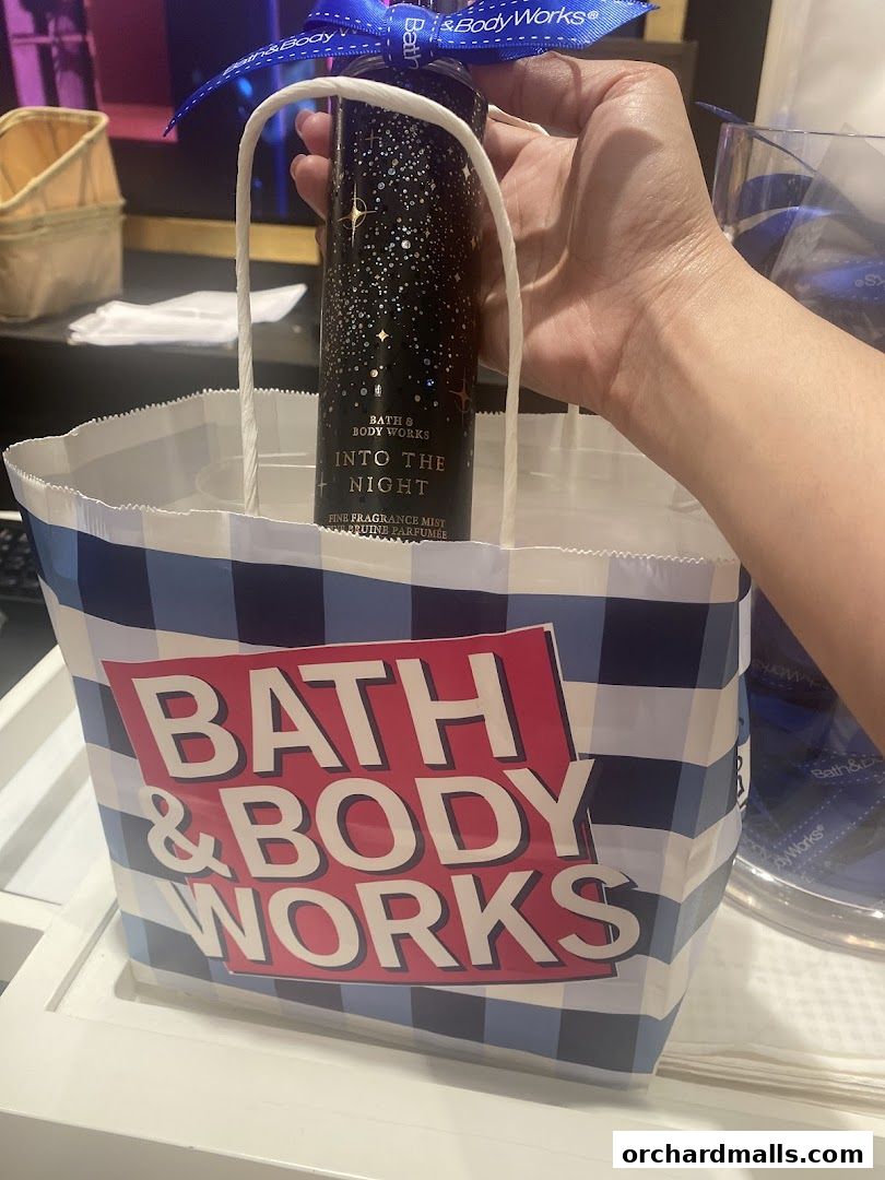 A hand holds a Bath & Body Works bag with a fragrance mist inside.
