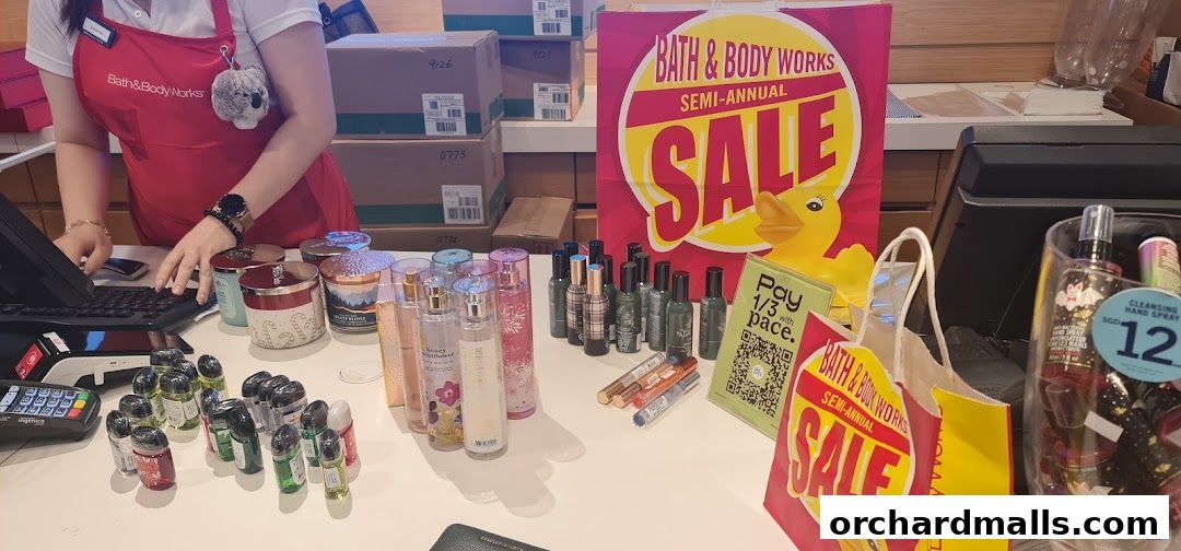 Bath & Body Works store counter with sale banners, candles, and various body care products.