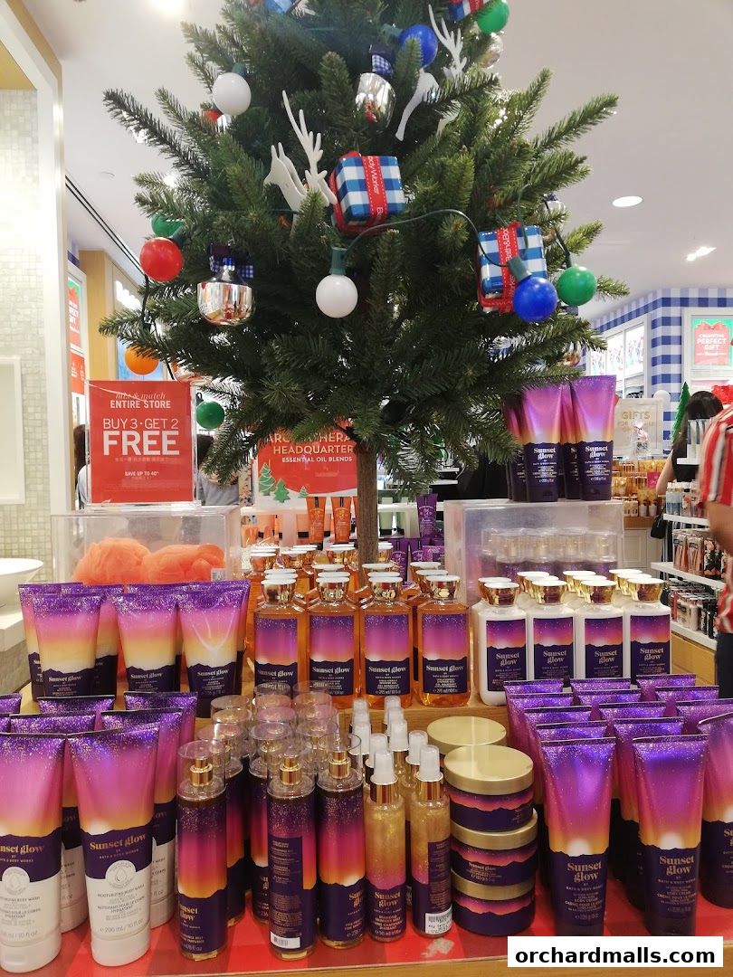 Bath & Body Works store display featuring 'Sunset Glow' products and a festive Christmas tree.