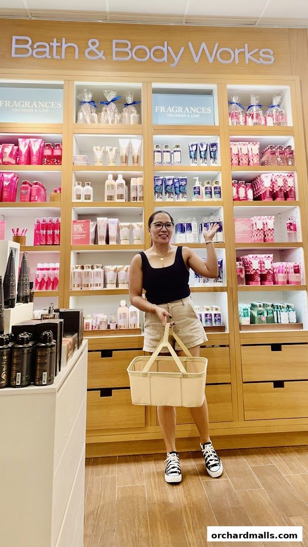 A woman poses in front of shelves stocked with Bath & Body Works fragrances and lotions.