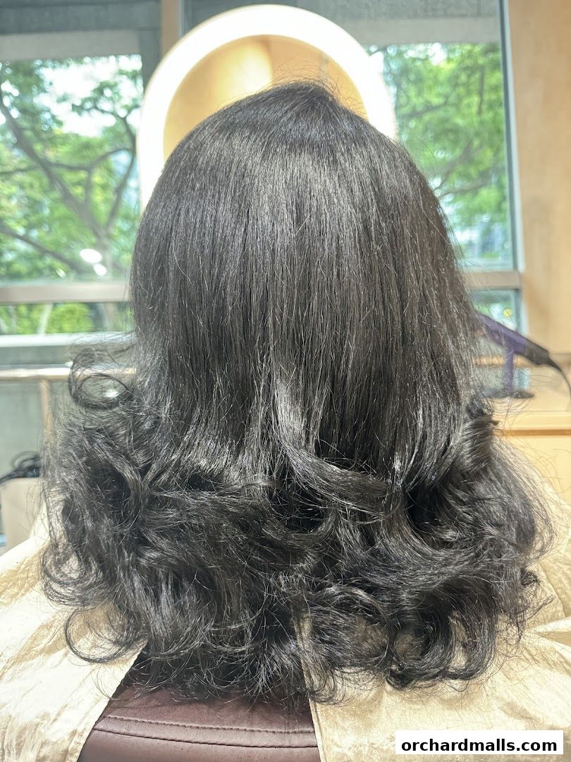 Back view of a person with long, dark, styled hair in a salon.