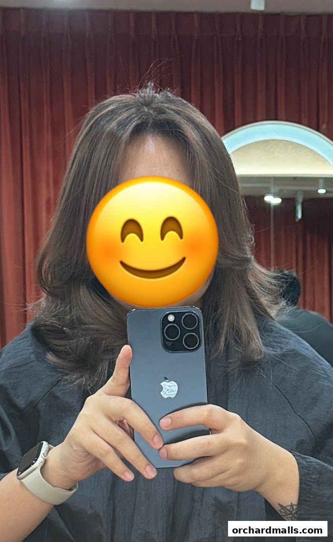 A person with a smiley face emoji covering their face takes a selfie in a salon.