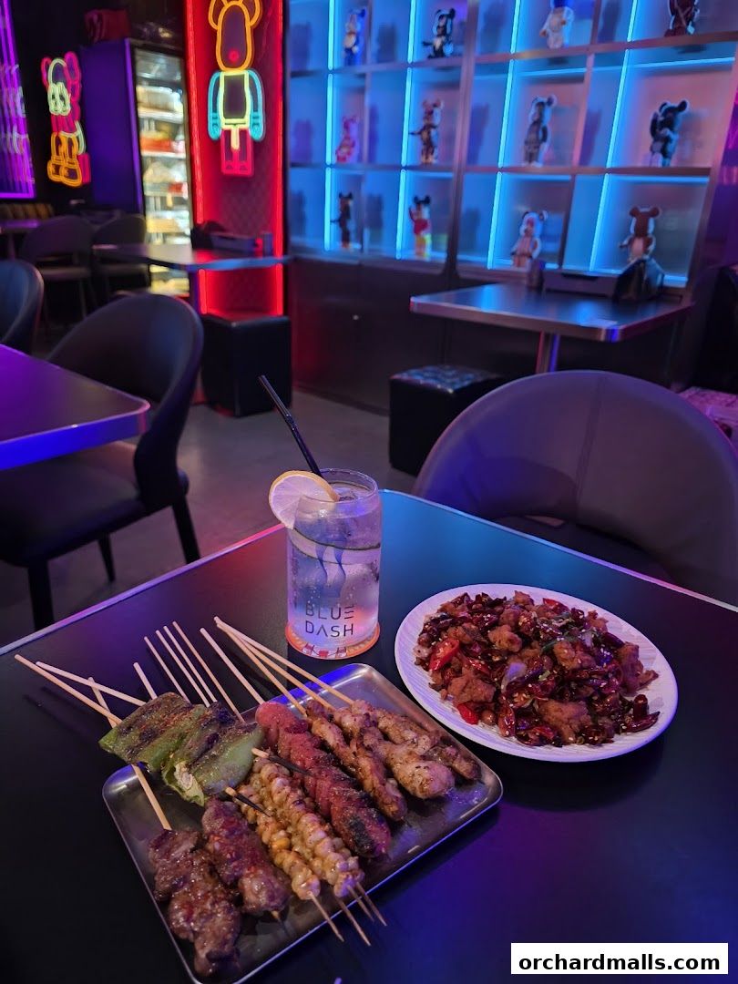 A table with skewers, a dish of fried food, and a drink in a neon-lit restaurant.