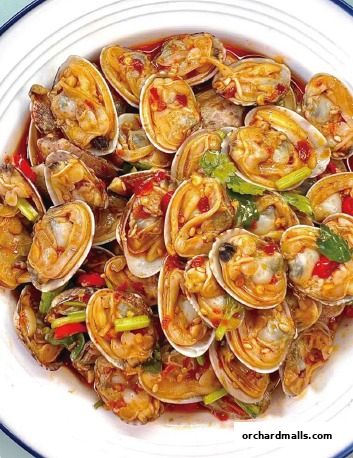 A close-up shot of a delicious dish of clams in a savory sauce with chili and herbs.