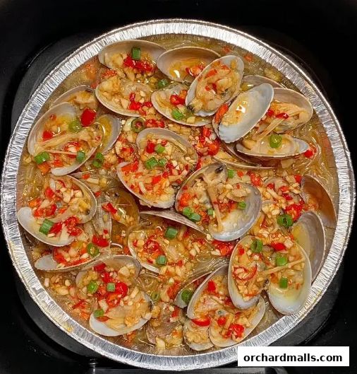 A close-up of steamed clams with chili, garlic, and scallions in a foil container.