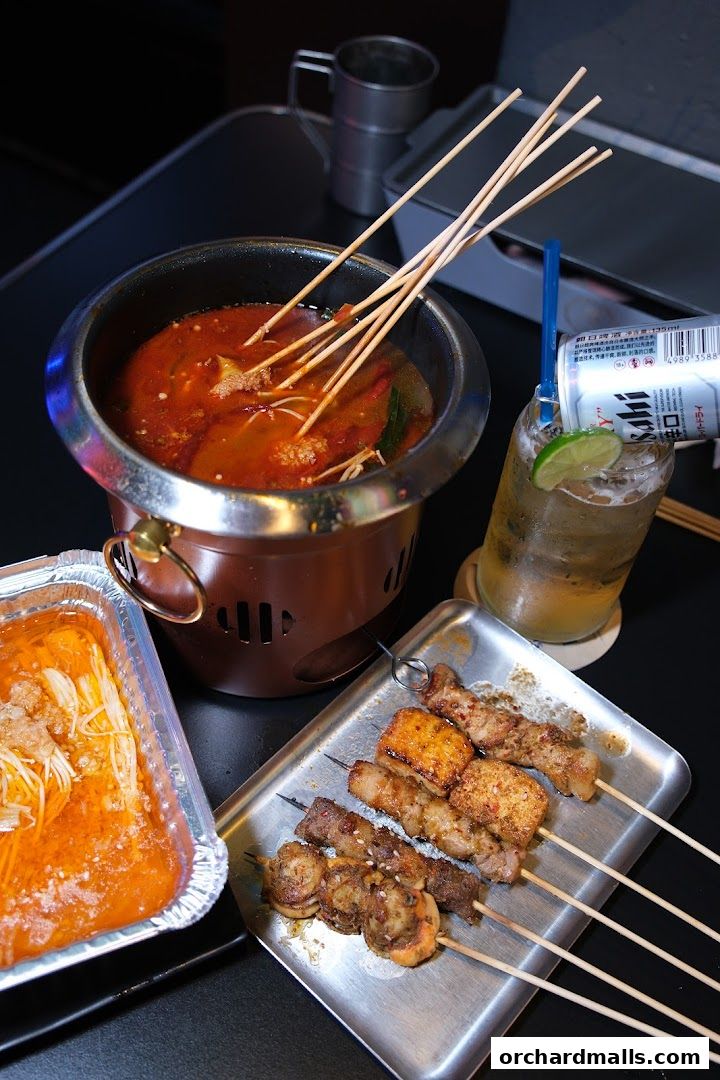 A table with a hot pot, skewers of meat and seafood, and a drink.