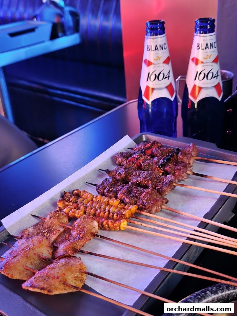 A tray of assorted grilled skewers and two bottles of 1664 Blanc beer.