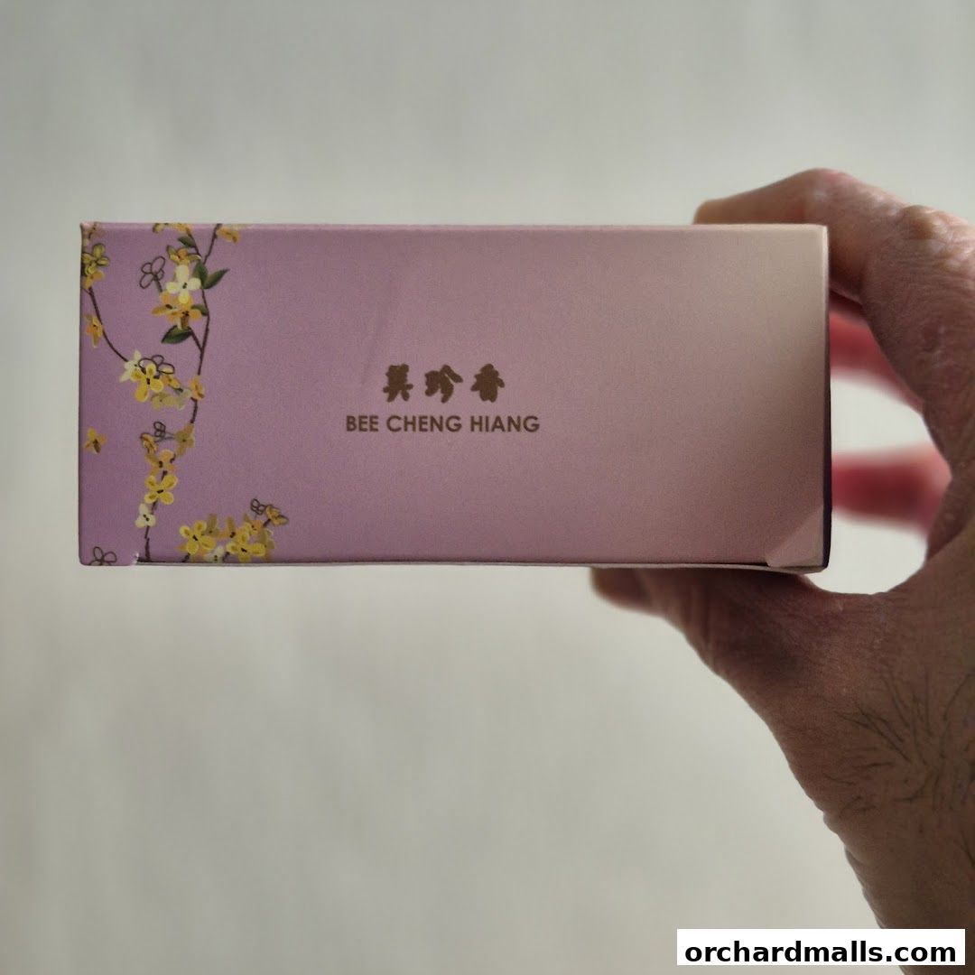 A hand holds a pink box with floral designs and the Bee Cheng Hiang logo.