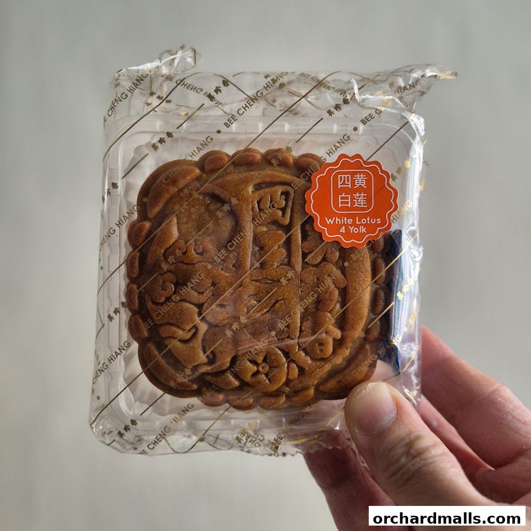 A hand holds a packaged mooncake with intricate designs and a label indicating 'White Lotus 4 Yolk'.