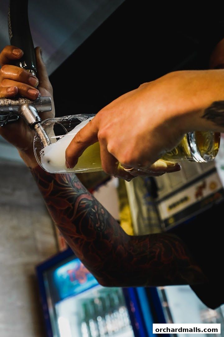 A bartender pours beer from a tap into a glass, showcasing tattooed arms.