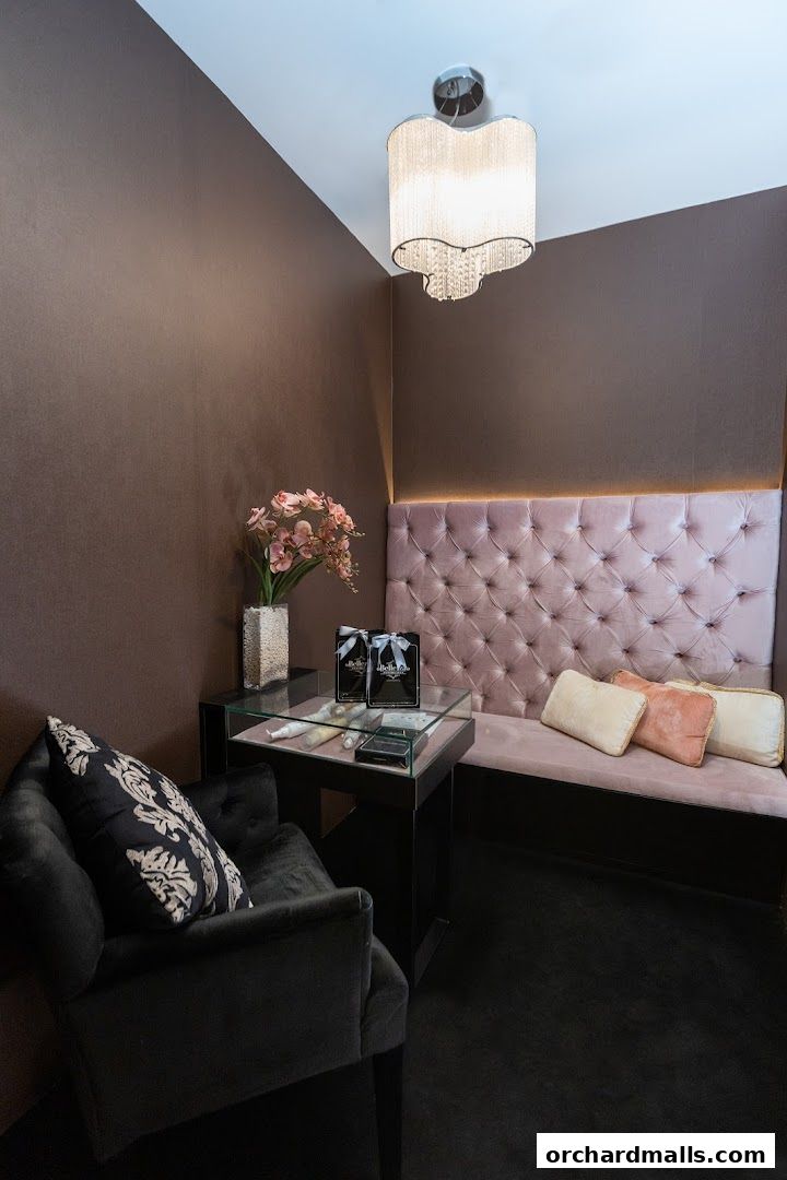 A luxurious waiting area with a tufted pink bench, plush chairs, and display cases.