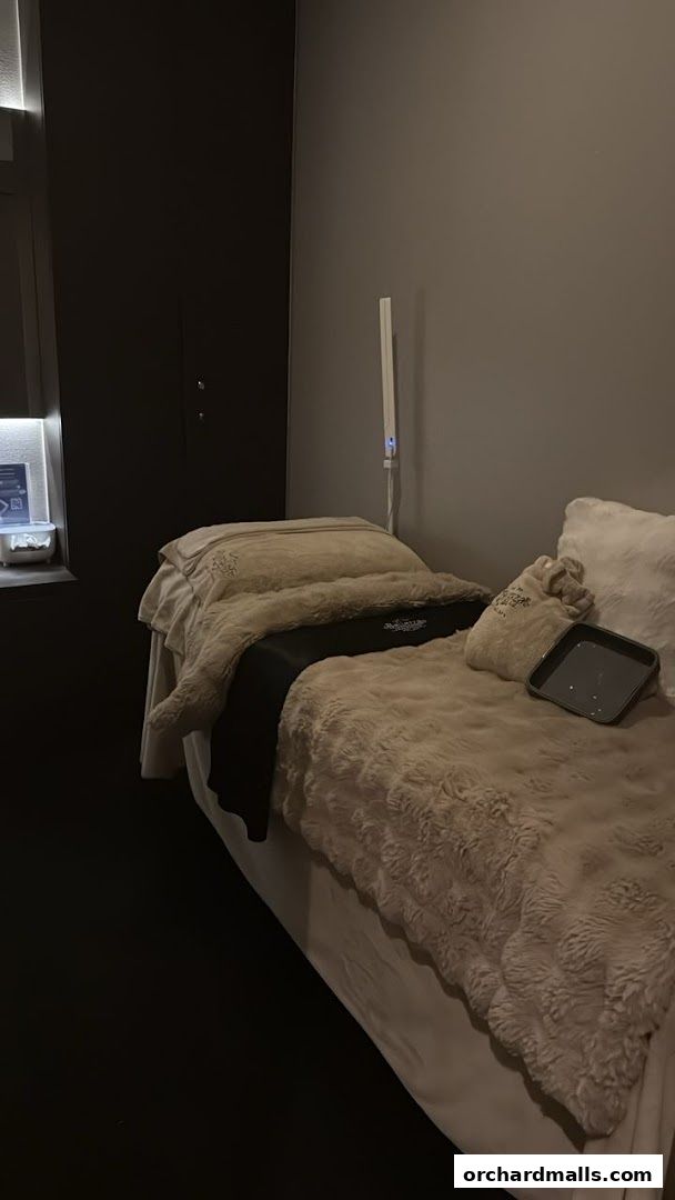 A treatment bed covered in plush blankets in a dimly lit aesthetic room.