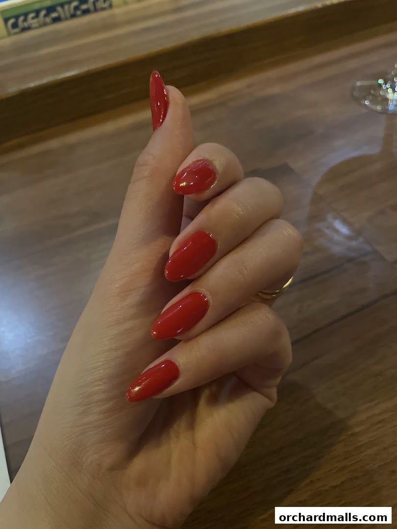 A hand with perfectly manicured, glossy red almond-shaped nails.