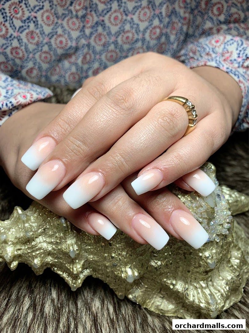 Close-up of hands with elegant ombre-style acrylic nails and a diamond ring.