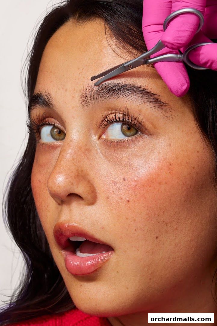 A close-up of a woman's face as her eyebrows are trimmed with scissors.