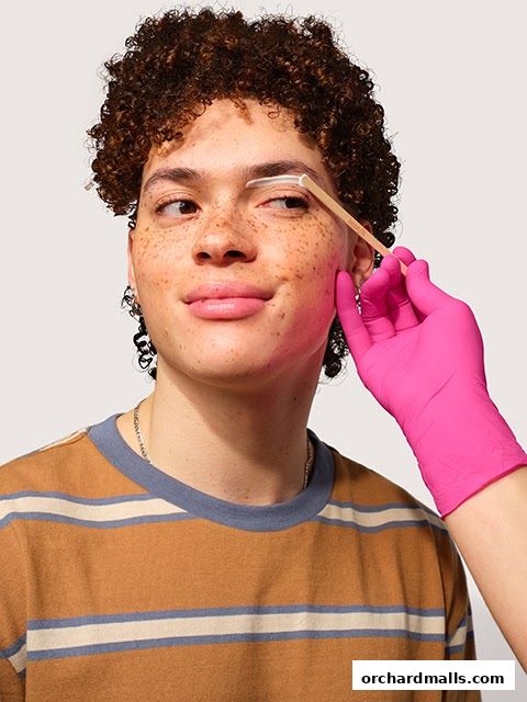 A person's eyebrow is being shaped with a tool and product by a gloved hand.