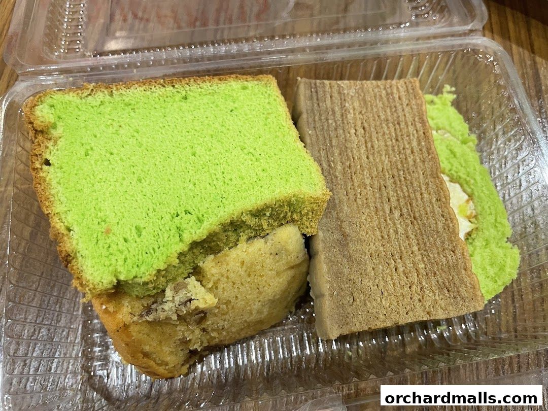 A clear plastic container holding slices of pandan cake and a log cake.