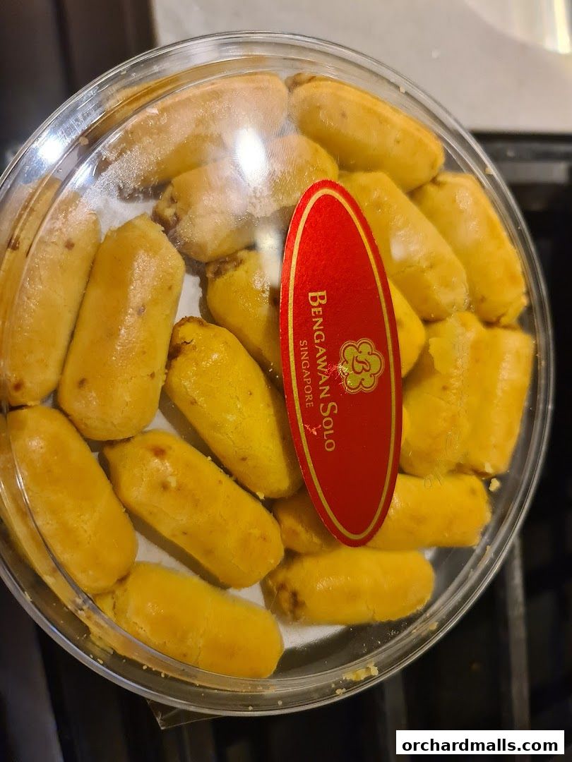 A clear plastic container filled with golden-brown, bite-sized cookies with a red label.