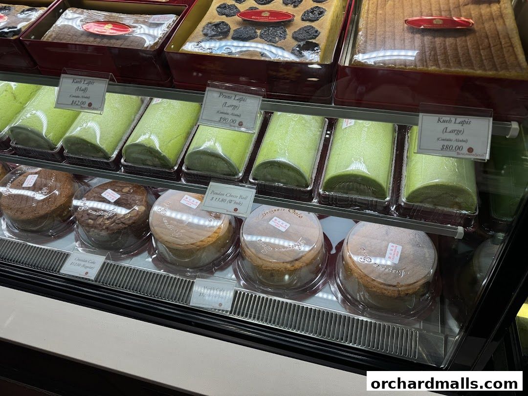 A display case filled with various cakes and rolls, with price labels visible.