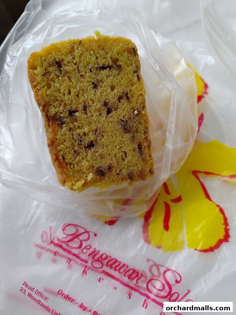 A slice of chocolate chip cake is presented in a plastic bag with the shop's logo.