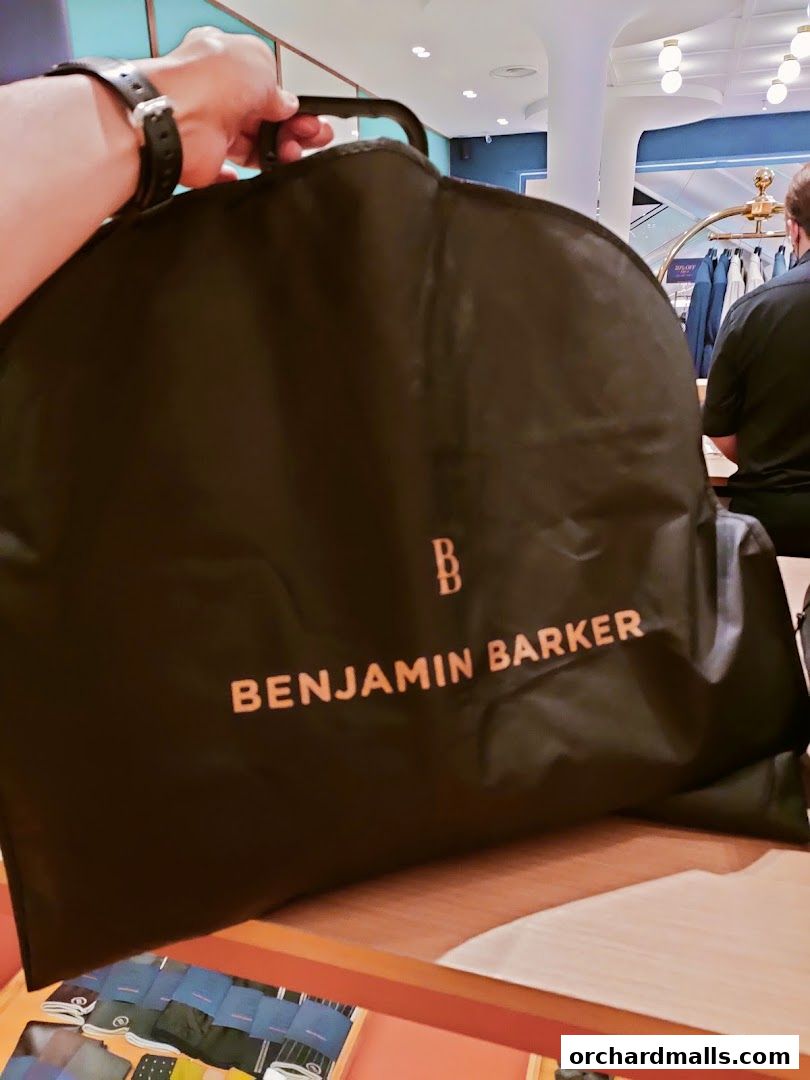 A hand holds a garment bag with the Benjamin Barker logo inside a store.