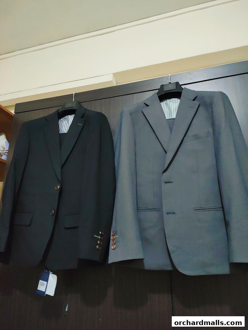 Two tailored suits, one black and one grey, are displayed on hangers.