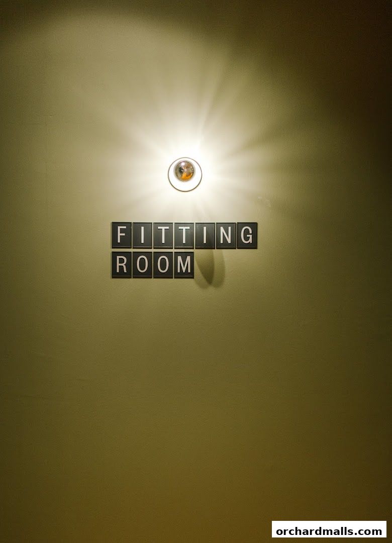 A sign reading 'FITTING ROOM' is illuminated by a spotlight on a textured wall.
